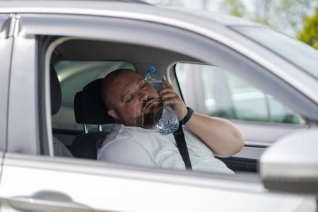 Photo for Exhausted fat overheat man with close eyes inside car with bottle of water on neck suffering from high blood pressure. Unhealthy overweight male feeling indisposition after traffic jam in hot weather. - Royalty Free Image
