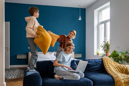 Photo for Work-family balance. Mother juggling working from home with looking after children, combining remote work with spending more time with family. Mom using laptop while her kids playing on background - Royalty Free Image