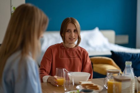 Photo for Mother eats breakfast and talks daughter about school. Family morning ritual. Young girl tells mom about lessons, share secrets. Trusting relationship between teenager and parent - Royalty Free Image
