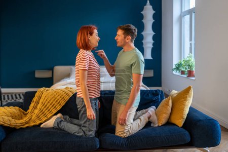 Photo for Negative emotions couples. Husband and wife arguing and shouting, expressive, emotional quarrelling home standing on couch. Man and woman kneeling front of each other. Male aggressively pokes female - Royalty Free Image
