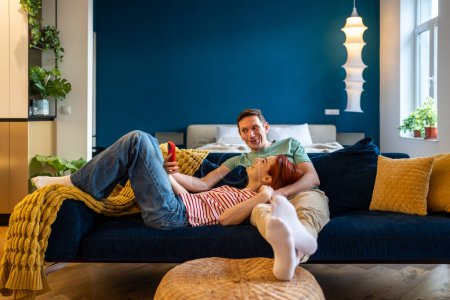 Photo for Family couple man woman making selfie on smartphone looking at screen sitting and lying on couch in modern apartment. Happy wife and husband photographing on phone laughing and smiling. Rest relax. - Royalty Free Image