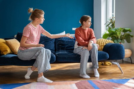 Conflict between parent and child. Teenage girl sits on couch facing away from toxic mother who retrieving child. Not understanding between daughter and mother, problems in family