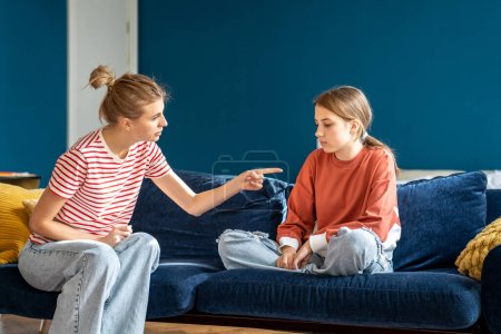 Photo for Angry mother pointing upset child sitting on sofa in living room. Conflict children and parents.Toxic mom humiliates young girl for bad behavior. Difficulties in raising teenage daughter - Royalty Free Image