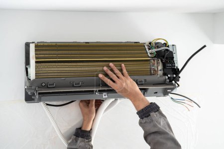 Photo for Hands of man technician in uniform installing air conditioner in apartment on wall. Maintenance and repair service concept. Creating pleasant microclimate for living. Climate control, split system. - Royalty Free Image