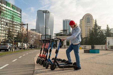 Photo for Man hipster choosing electric scooter for rent in city park activating using smartphone. Modern way to move in urban environment. Eco friendly transport. Public ecology alternative transportation. - Royalty Free Image
