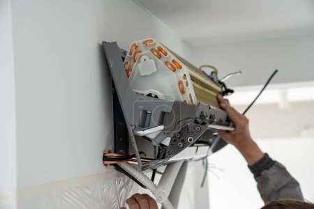 Téléchargez les photos : Les mains de l'homme technicien en uniforme installation climatiseur dans l'appartement sur le mur. Service d'entretien et de réparation concept. Créer un microclimat agréable pour vivre. Régulation de la température, système split. - en image libre de droit