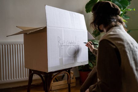 Photo for Ecological activist girl signs cardboard box for things be recycled. Zero waste care for environment. Reasonable consumption, waste sort. Choice people save planet. Green volunteer preparated trash - Royalty Free Image