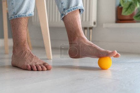 Foto de Hombre que utiliza bola de silicona para el masaje de pies durante el trabajo sedentario largo, las piernas de cerca. Ejercicios físicos para la recuperación de los pies después de lesiones traumáticas, mejora de la circulación sanguínea, prevención de enfermedades de las piernas. - Imagen libre de derechos