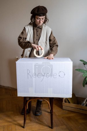 Photo for Interested girl eco activist seals box with inscription recycle. Sorting out wardrobe and getting rid of unnecessary. Reuse dress. General social activity. Green volunteer save planet from trash. - Royalty Free Image