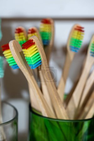 Photo for Eco friendly bamboo toothbrushes with recycled plastic bristles of different color in glass tumblers. Biodegradable ecological personal care products. Plastic free lifestyle, environmental protection. - Royalty Free Image