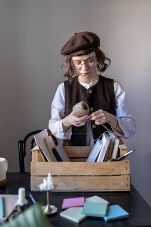 Photo for Workplace artist. Creative hipster girl holdsball of thread in hand, stands table and lays out art tools and drawing materials in wooden box. Brings order art tools. Artist prepares space for work. - Royalty Free Image