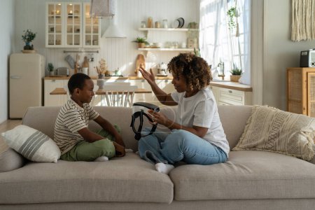Photo for Young African American mother holding VR helmet introducing virtual reality technology to child son while spending leisure time together at home. Mom parent exploring virtual world with kid - Royalty Free Image