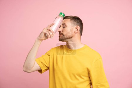 Photo for Overheated tired man puts bottle of cold water to forehead, suffers from heat and blood pressure. Exhausted guy trying to cool down after sports training in hot summer day, feels dehydrated or thirsty - Royalty Free Image