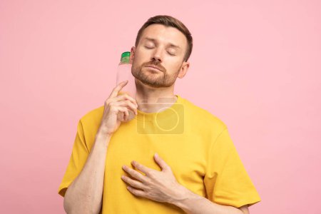 Photo for Overheated tired middle aged man suffers from heat, puts bottle of cold water to neck. Exhausted guy trying to cool down after sports training in hot summer day, feels dehydrated and thirsty. - Royalty Free Image
