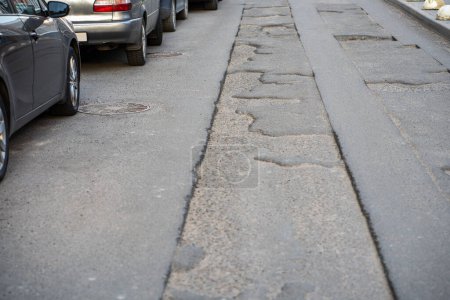 Photo for Broken asphalt road in city and untimely repair in parking lot. Pothole asphalt road repairs. Patched roadway in bad condition. Prolonged repair of urban infrastructure. Cars parked on side of road. - Royalty Free Image
