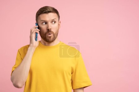 Photo for Surprised man smartphone talk feeling awed open mouthed shocked looks to empty space for dream isolated on pink background. Wow, look here. Excited male showing eyes place for advert promotional text. - Royalty Free Image