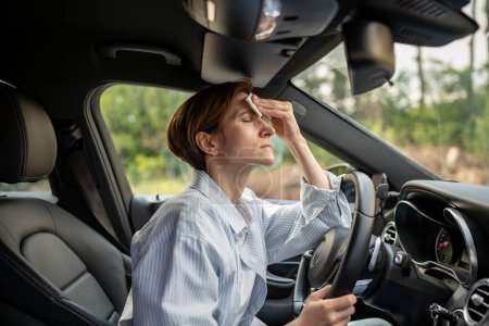 Photo for Woman drives car with broken air conditioning in hot summer weather. Wipes sweat paper napkin. Middle aged female suffering from heat stuffiness, high temperature, humidity. Overheated worried driver. - Royalty Free Image