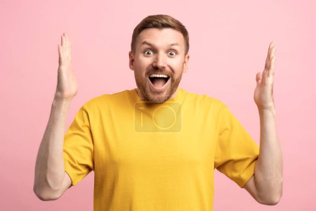 Photo for Overjoyed excited happy young man smiling with opened mouth looking at camera isolated on studio pink background rising hands up, winner gesture. Sincere human emotions, achieving life goal concept. - Royalty Free Image