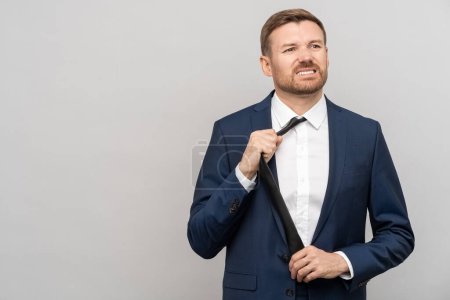 Photo for Overworked irritated employee manager pulls choke tie off neck isolated on studio background. Dissatisfied tired frustrated man angry from problems needs psychological help from professional burnout - Royalty Free Image