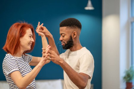 Photo for Happy loving young diverse couple dancing romantic dance in modern bedroom with panoramic windows. Smiling husband and wife celebrating anniversary, enjoying tender moment, having fun at home. - Royalty Free Image