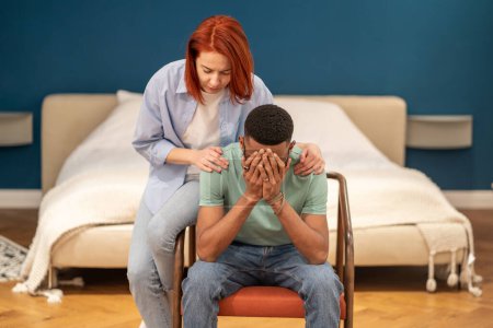 Photo for Unhappy diverse couple discussing divorce at home, husband feeling sad and frustrated after difficult conversation with wife. Loving girlfriend trying to comfort crying boyfriend embracing him - Royalty Free Image