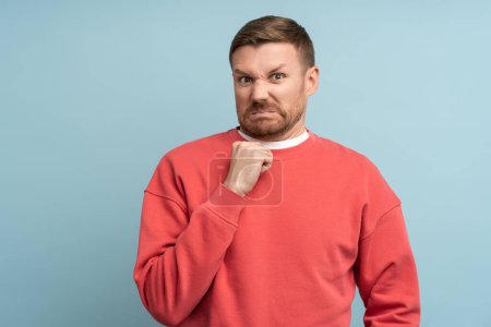 Photo for Emotion of disgust on face of young man. Middle aged male in red sweatshirt on blue background with bright expressive facial expressions looks at camera contemptuously with hostility, loathing. - Royalty Free Image