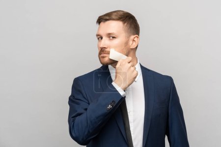 Photo for Office worker in suit peeling off tape from mouth on studio gray background looking at camera. Total subordination at work, lack of ones own opinion, prohibition of statements, censorship concept. - Royalty Free Image