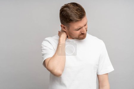 Photo for Unwell man frowns suffers from pain in neck isolated on grey studio wall. Inflammation of spinal discs hernia, sedentary lifestyle. Impact of overworking on male health. Physical problems in adulthood - Royalty Free Image