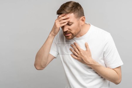 Photo for Unhealthy middle aged man presses hand to chest and head having heart pain, headache. Male suffering from heart attack isolated on gray wall. Health breath problems, heartache, high blood pressure. - Royalty Free Image