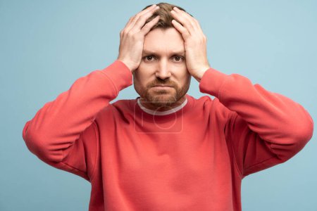 Photo for Anxiety sad man holds head thinks about difficult troubles in life, incorrect choice, lack of money on blue studio background. Worried depressed middle age male suffering from mistake feel frustration - Royalty Free Image