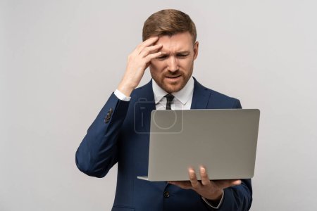 Photo for Frustrated businessman in emotional stress watching downfall stock market on laptop, lost money on falling stock prices. Furious trader man in costume think about problem isolated on studio gray wall. - Royalty Free Image
