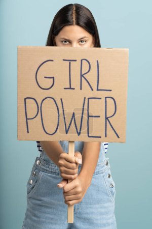 Photo for Feminist holds banner girl power. Serious strong message to society, appeal to misogynistic anti-feminist communities. Woman protests, fights for rights of girls. Vertical photo, isolated on blue. - Royalty Free Image