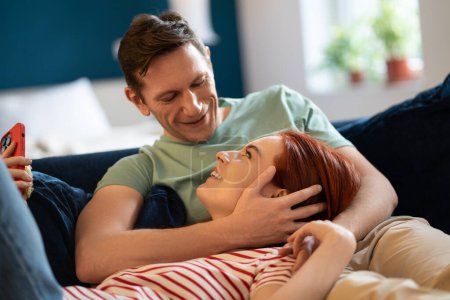 Photo for Well rested couple lovingly look at each other sharing care relaxing lying on sofa. Positive middle aged family lies embracing at home. Happy man and woman spend time together, make plans for future - Royalty Free Image