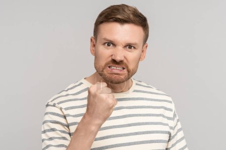 Photo for Angry aggressive bearded man clenched fist has evil face looking at camera on grey background. Madly furious guy viciously threatens assault, reprisal or attack. Sincere negative emotions concept. - Royalty Free Image