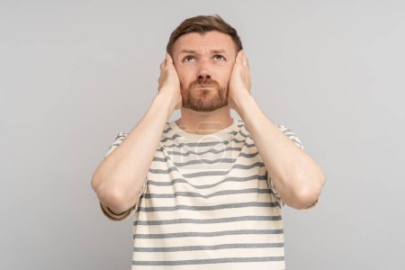 Photo for Tensed confused desperated man clutched cheeks looking up on grey background. Advertisement banner, poster for sale, marketing concept. Frustrated guy feels negative emotions has problems, troubles. - Royalty Free Image