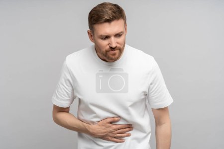 Photo for Unhealthy exhausted man feeling stomach ache writhing in pain isolated background. Diseased middle aged male suffering from food poisoning, gastritis, pancreatitis, flatulence needs medical treatment. - Royalty Free Image