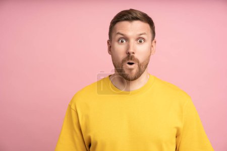 Photo for Amazed customer looks at camera in shock astonishment mouth open. Agitated man surprised with big eyes, numb to hear secret information. Shocked caucasian guy gossip news reaction isolated on studio - Royalty Free Image