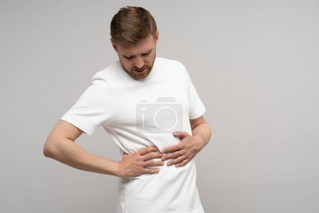 Photo for Ache in right side. Sick man suffering from discomfort under ribs, feels sharp pain, isolated background. Diseased male writhing in acute abdominal pain needs treatment. Inflammation, appendicitis. - Royalty Free Image