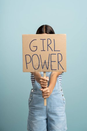 Téléchargez les photos : Femme manifestante tenant du carton recyclé avec le slogan girl power. Fille adolescente féministe méconnaissable avec signe d'autonomisation isolé sur fond bleu studio. Concept des droits des femmes. - en image libre de droit