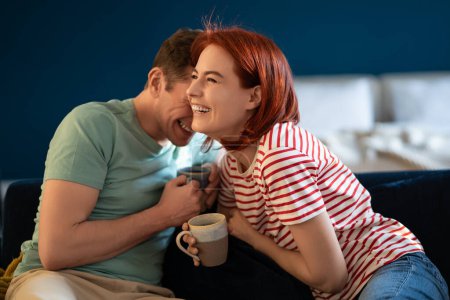 Photo for Well-rested couple talking and laughing. Middle aged smiling wife and husband sitting with cup tea morning on sofa. Loving family having fun weekend. Emotional connection in healthy relationship. - Royalty Free Image