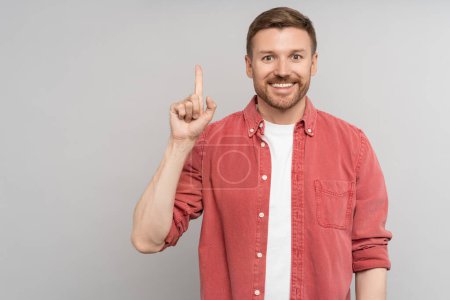 Photo for Look over there. Satisfied smiling man pointing up presenting product looking at camera. Handsome happy guy with idea gesture showing direction with finger isolated studio background. Copy free space - Royalty Free Image