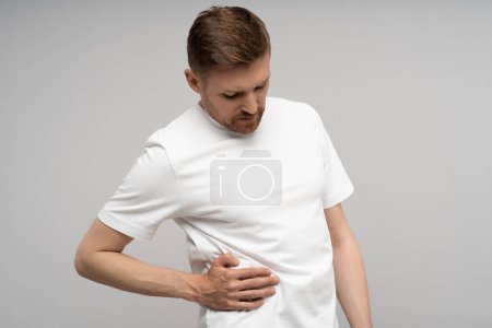 Photo for Man feeling unwell, pain in right part of abdomen, suffering from spasms on grey background. Stomach intestine ulcer, stomachache, gastritis, abdominal pain, indigestion, health problems concept. - Royalty Free Image