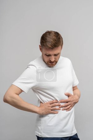 Photo for Man having health problems feeling pain spasms in right part of body on grey background. Stomachache symptom, abdominal painful concept. Appendicitis, inflammation of appendix, sharp pain, ache hurt. - Royalty Free Image