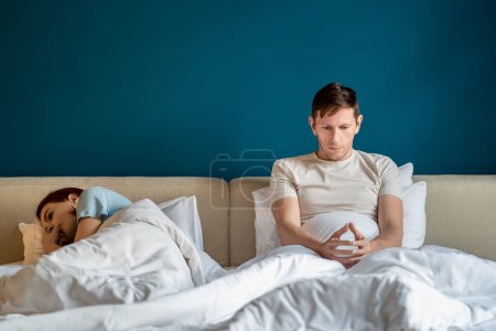 Photo for Thoughtful sad man woman in bed feeling despair after quarrel at home. Husband sits looks at hands, wife turned away lying near. Misunderstanding, problem relationships, marital discord, ignoring. - Royalty Free Image