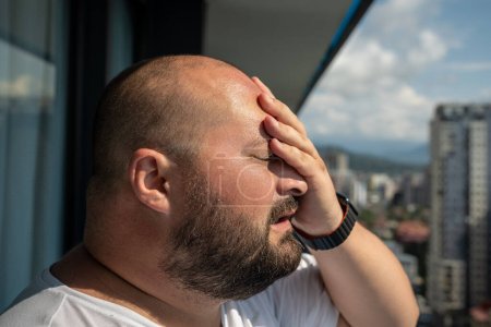 Photo for Portrait overweight man has headache touching forehead in heat summer weather. Bearded guy with excess weight closed eyes stand on balcony. Extra high temperature, health problems concept. - Royalty Free Image