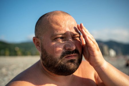 Photo for Bearded overweight man looking at distance on nature at sunny weather covering eyes from sun in summer. Portrait of male resting outdoors, basking with naked torso. Rest, relax, spend time on beach. - Royalty Free Image