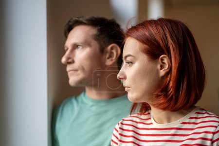 Photo for Unsmiling man and woman look out window. Guy and girl, young romantic married couple seriously watching what happening outdoor frustrated disappointed by cloudy cold weather outside. Close up portrait - Royalty Free Image