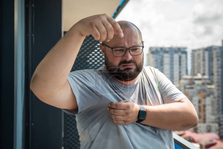 Photo for Man with wet armpits and disgusted expression on face. Fat obese young guy with glasses suffering from severe sweating, overweight. Humid climate and high air temperature in city in hot summer. - Royalty Free Image