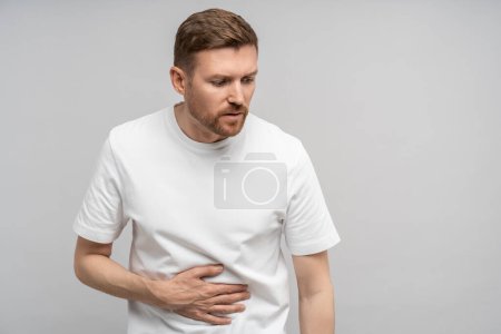 Man holds on to sore stomach. Unwell guy experiences nausea, suffers from symptoms of gastritis, acute pain in stomach, intestines, discomfort, unpleasant feeling, ache in abs after exercise, sports.