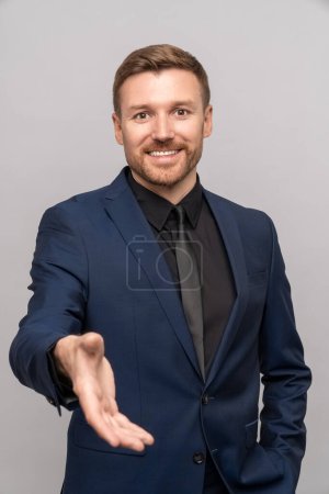 Photo for Smiling businessman holds out hand, offering to make deal, isolated background. Confident man in business suit extends palm for handshake, merchant trader offers service, conclude profitable contract - Royalty Free Image